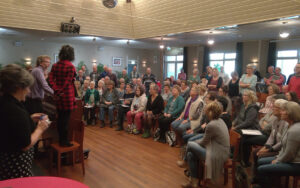 Gastzangers en zangers van Con Brio en Ettens Mannenkoor tijdens het inzingen bij Köster met dirigenten Nick Moritz en Armanda ten Brink (zoals vaak bij het inzingen staand op een stoel om ook de achterste rij te kunnen zien). Foto: Sjon Slutter